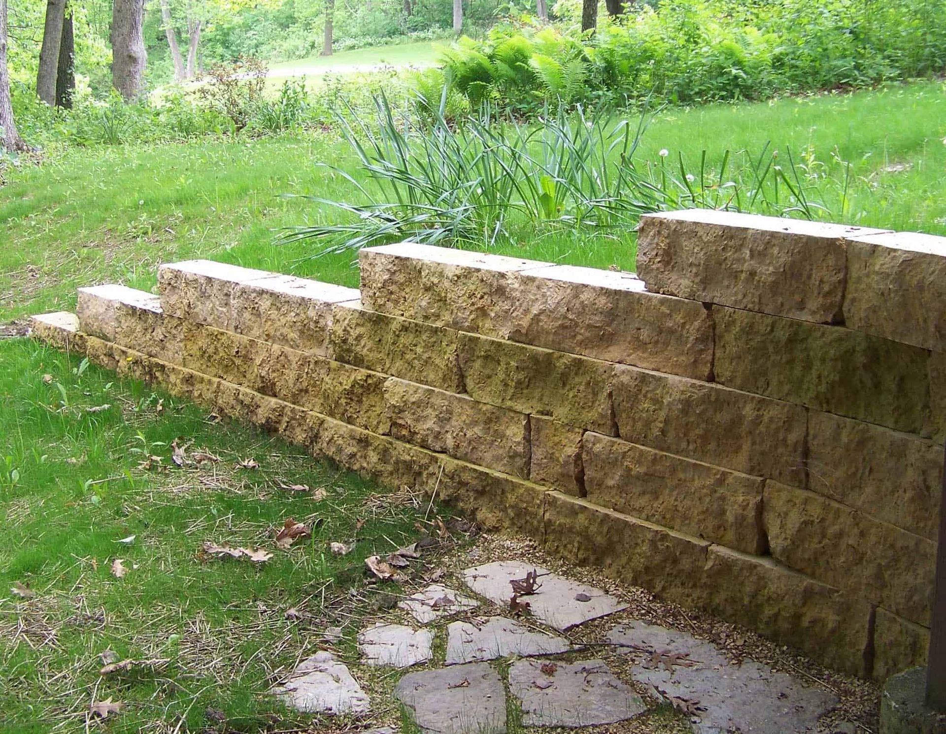 A stone wall is sitting in the middle of a lush green field.