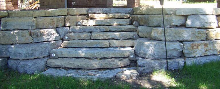 A stone wall with stairs built into it in a yard.
