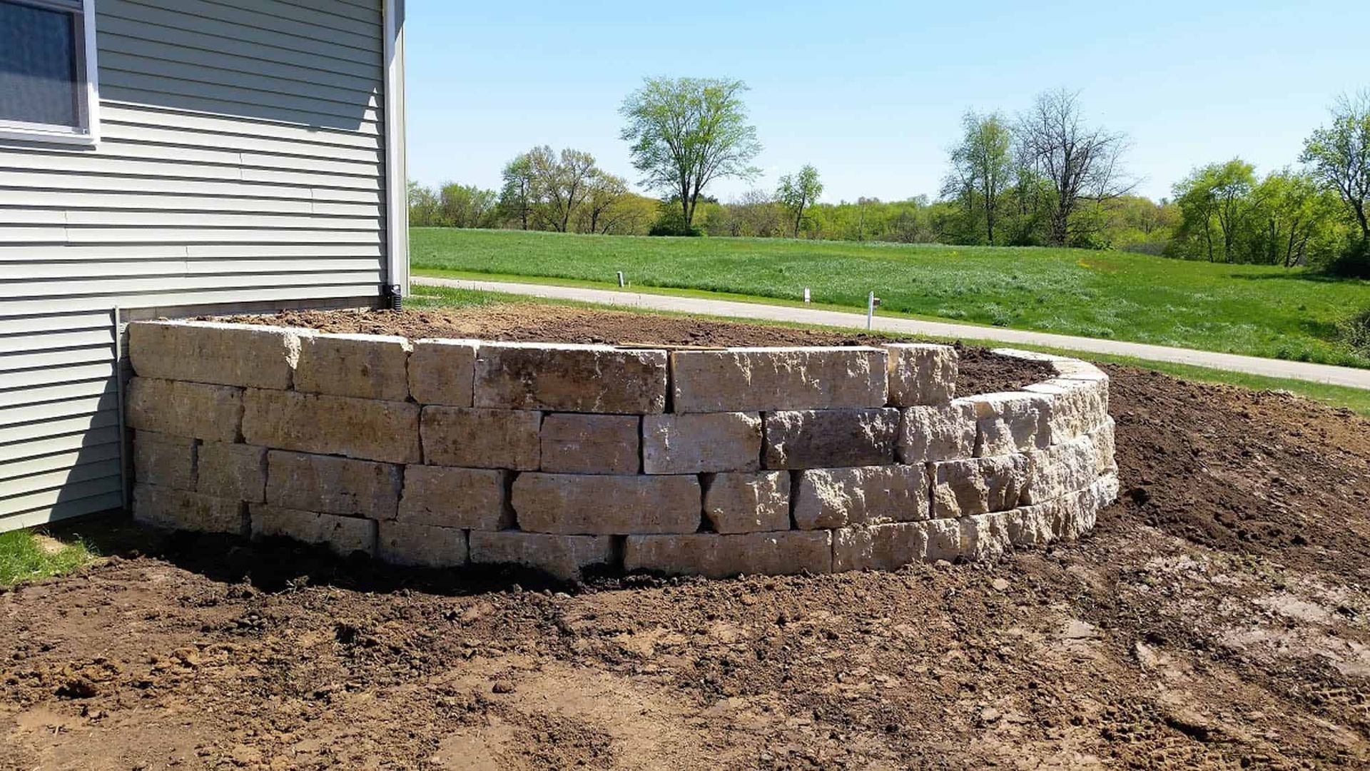 A stone wall is sitting in the dirt in front of a house.
