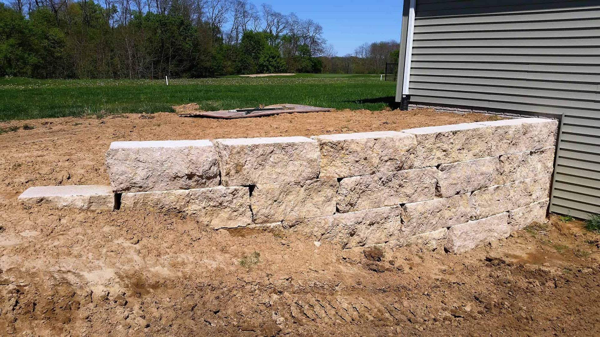 A stone wall is being built in the dirt in front of a house.