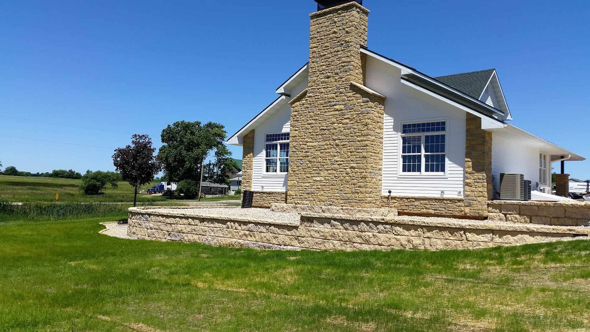 A white house with a stone chimney is sitting on top of a lush green field.