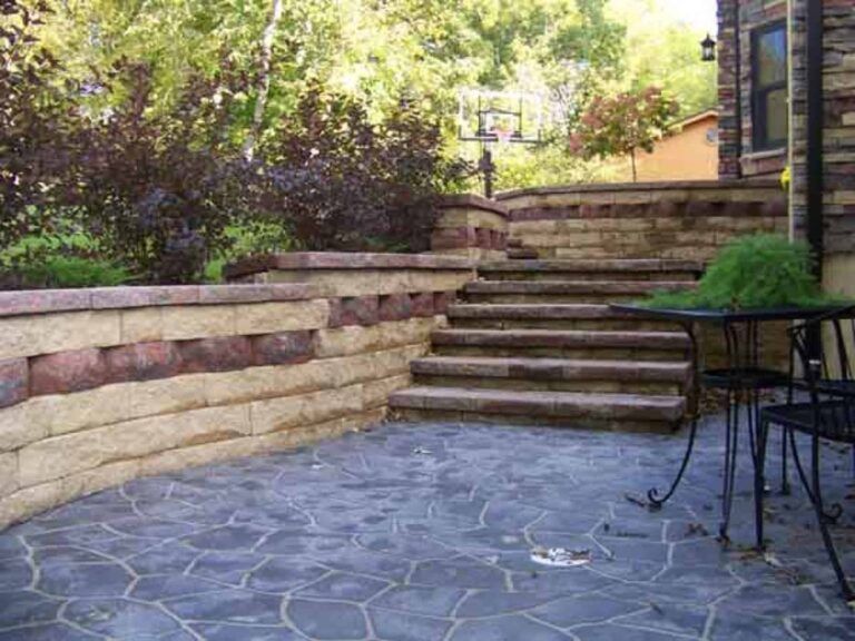 A patio with stairs and a table and chairs in front of a house.