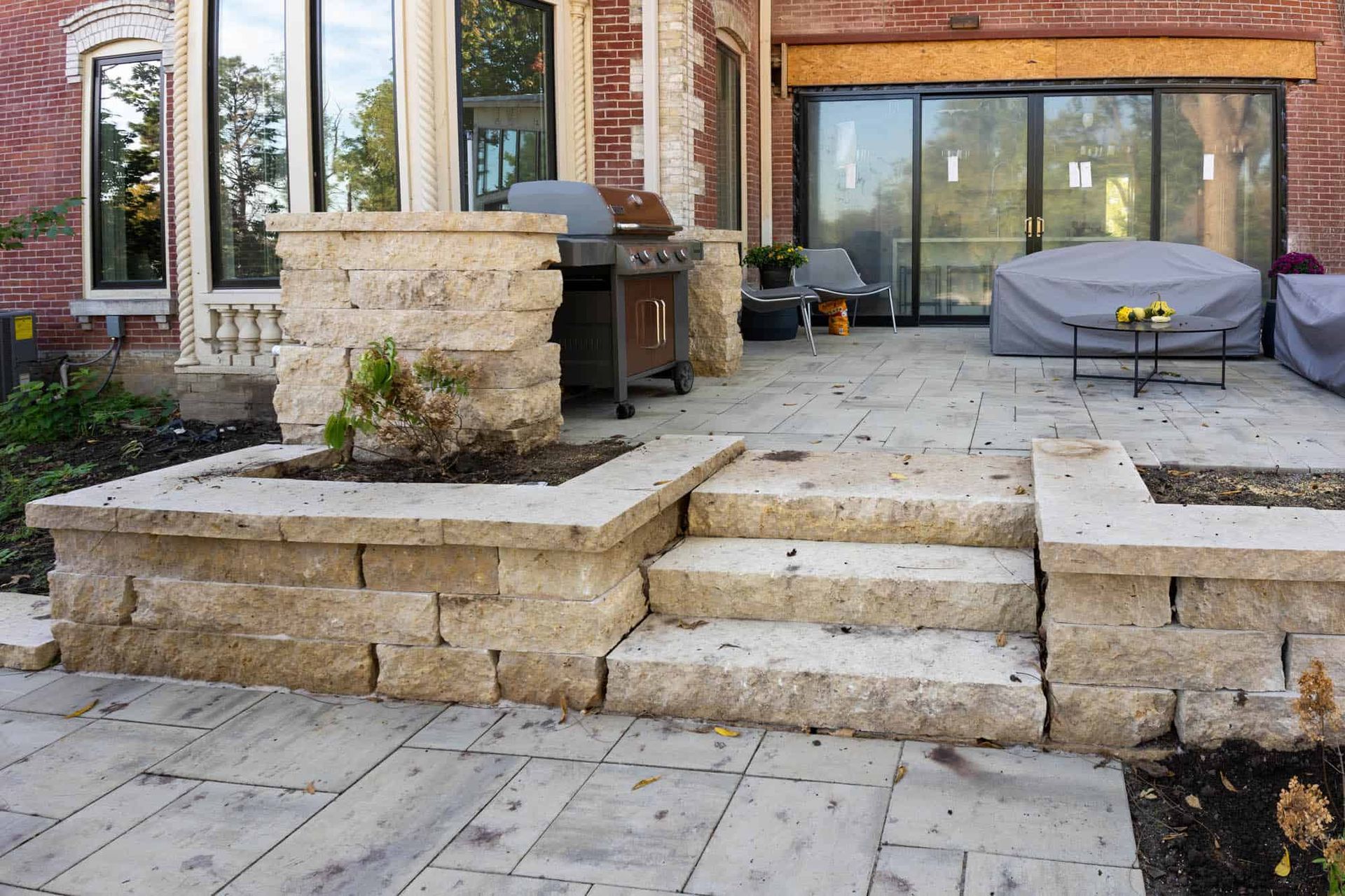A patio with stairs and a grill in front of a brick house.