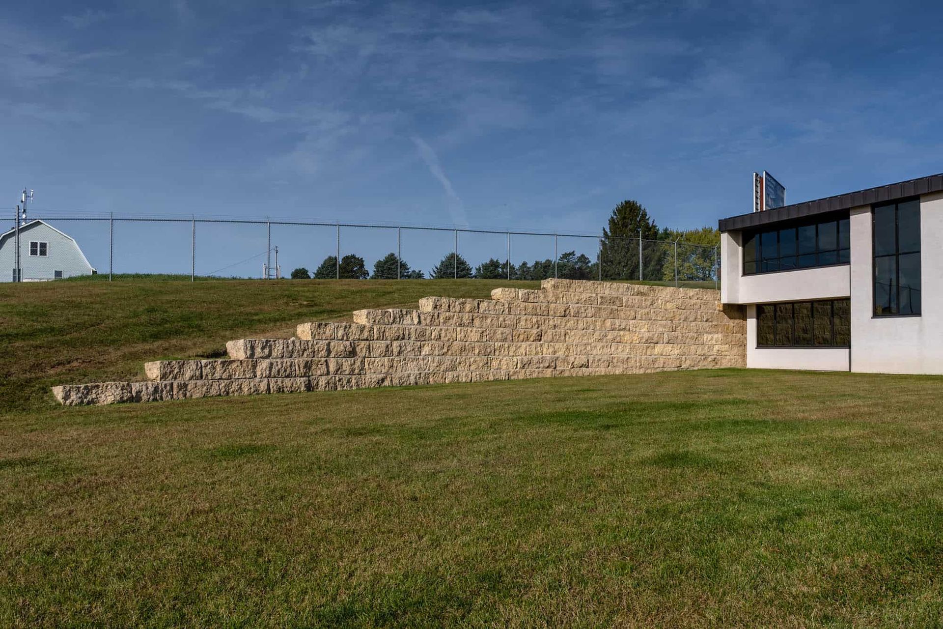 A large building is sitting on top of a grassy hill next to a stone wall.