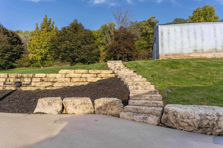 A stone wall with stairs leading up to a grassy hill.