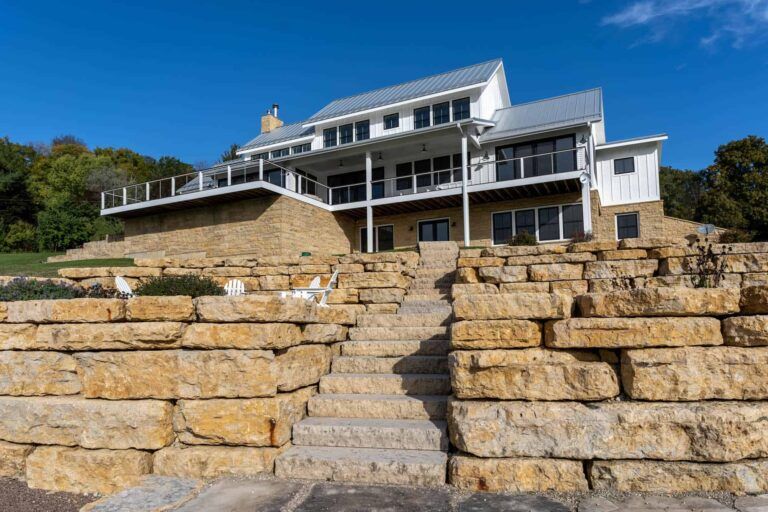 A large house is sitting on top of a hill next to a stone wall.