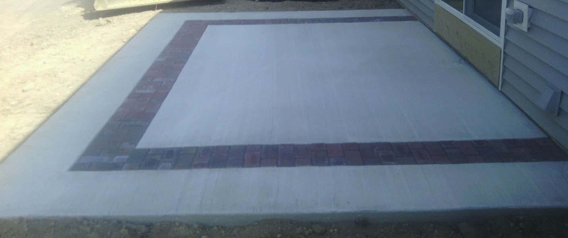 A concrete patio with a brick border is sitting next to a house.
