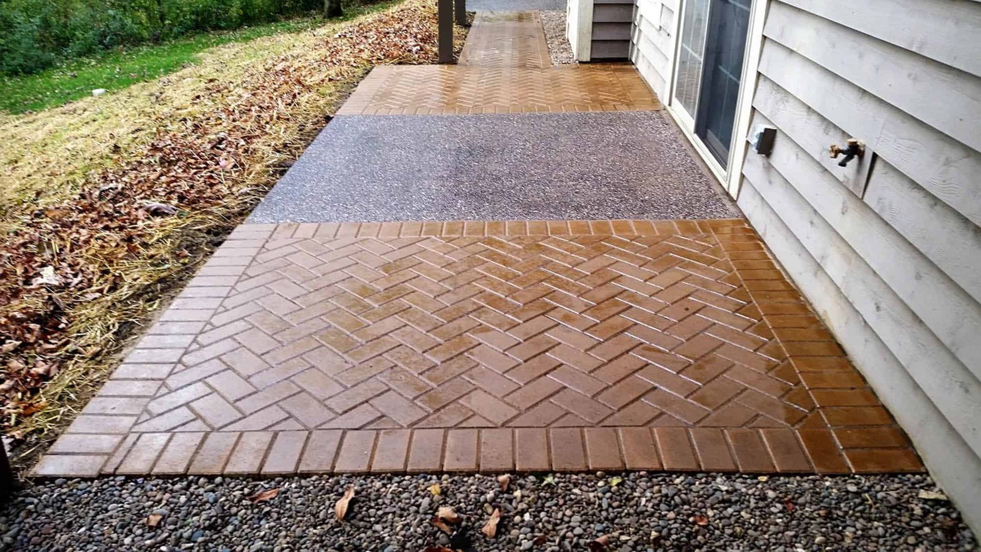 A brick walkway leading to a house with a herringbone pattern