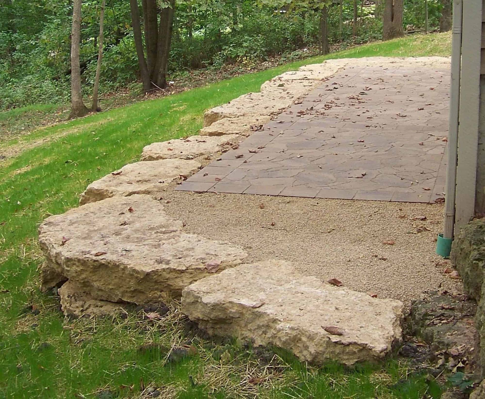A stone wall surrounds a gravel driveway in a yard