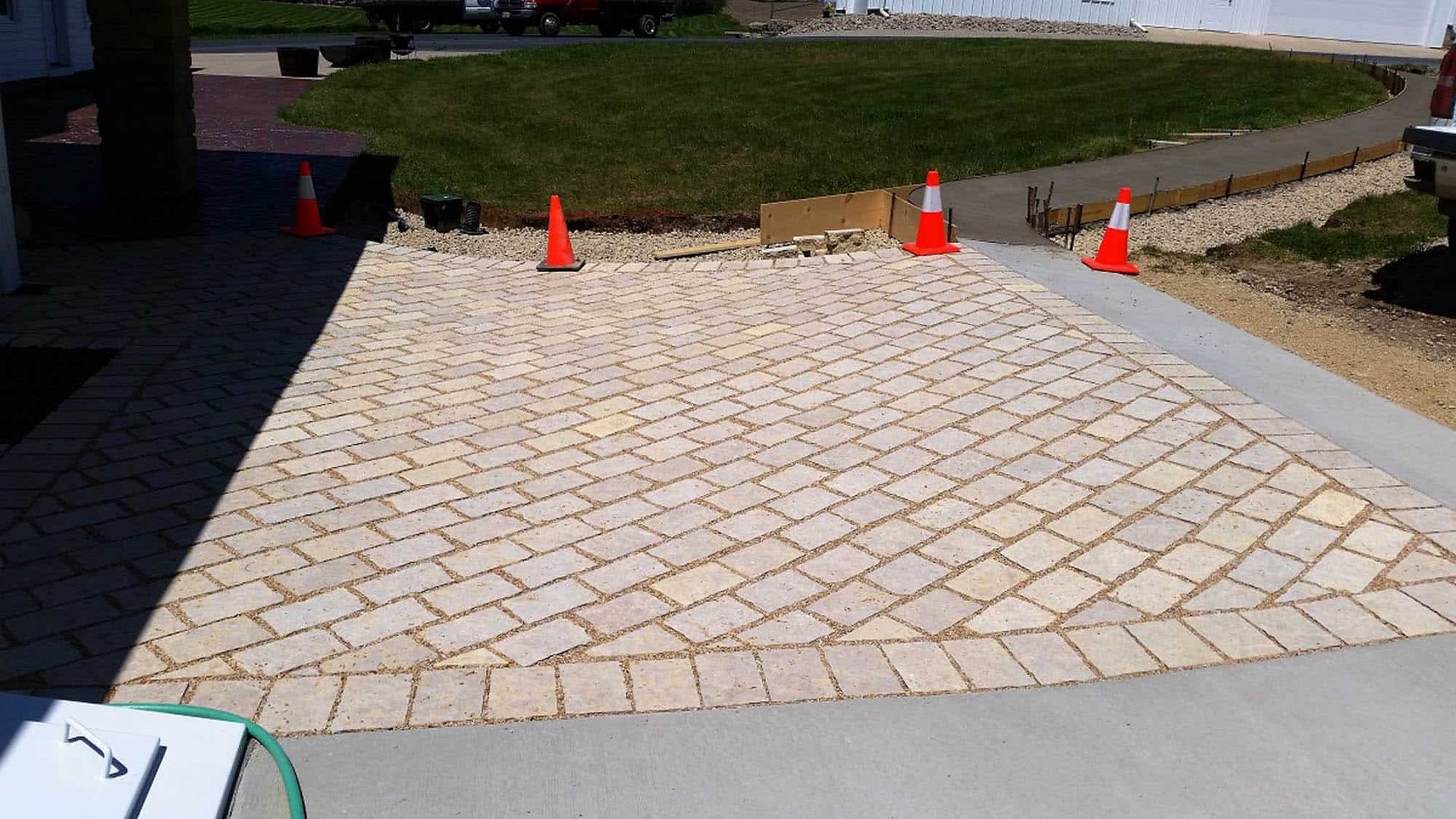 A brick driveway is being built with orange and white traffic cones.