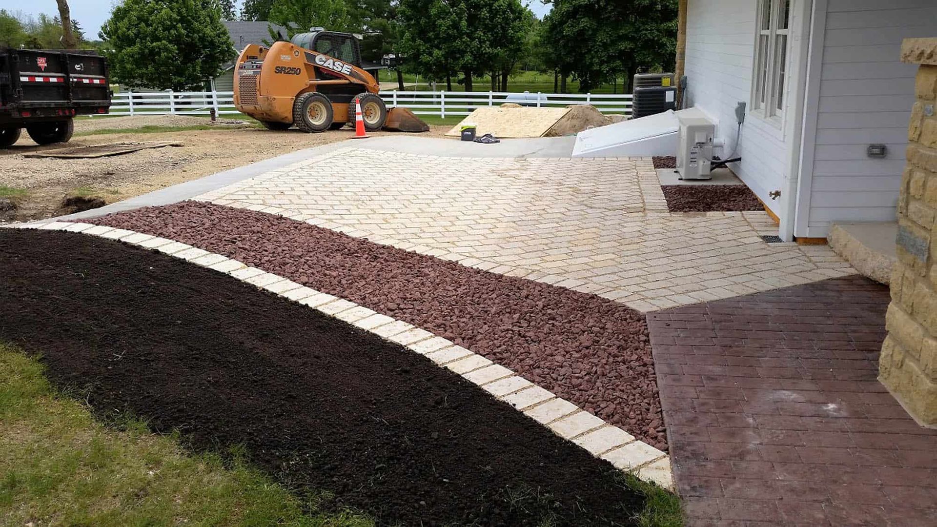 A tractor is working on a driveway in front of a house.