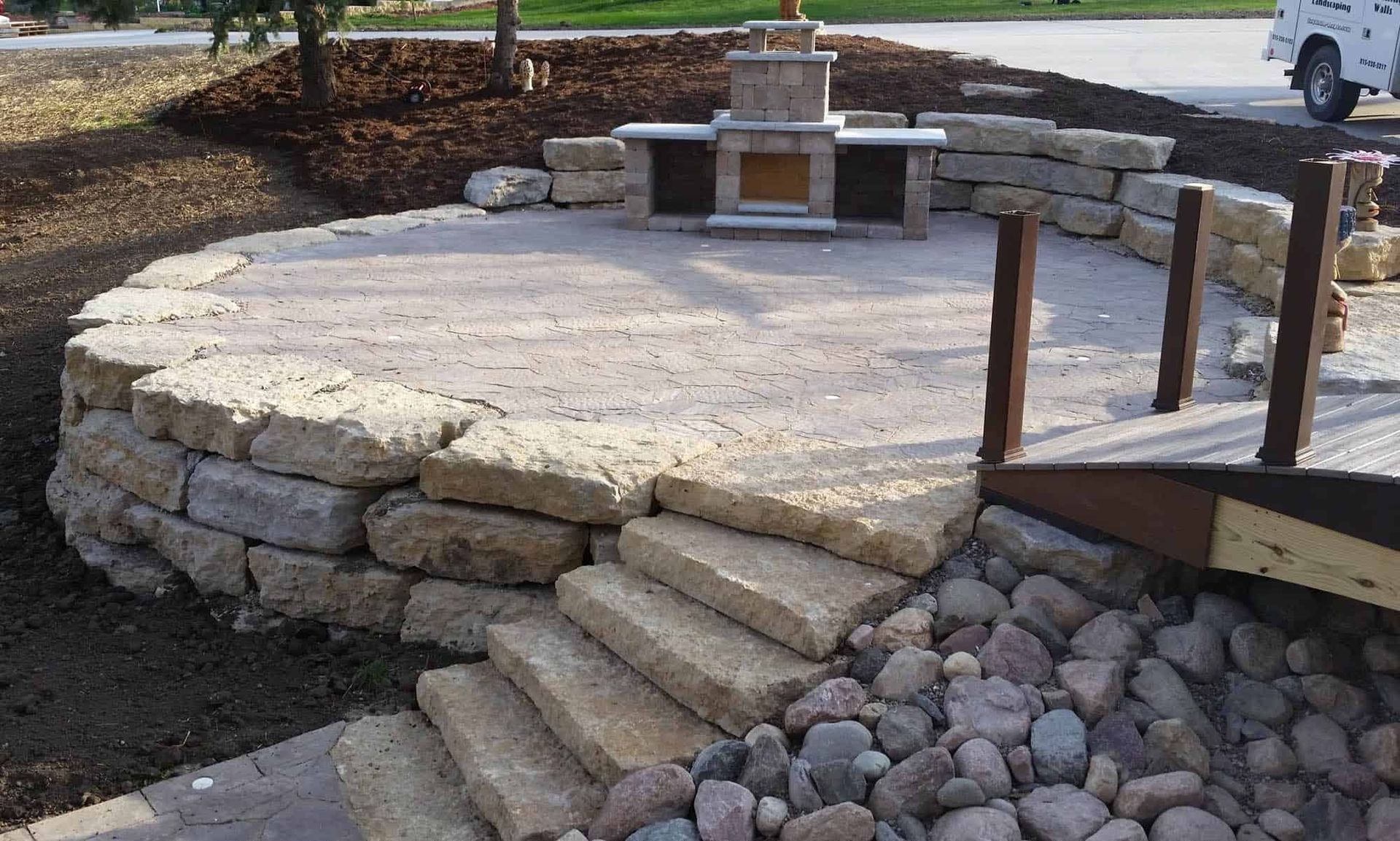 A stone patio with stairs leading up to it and a fireplace.