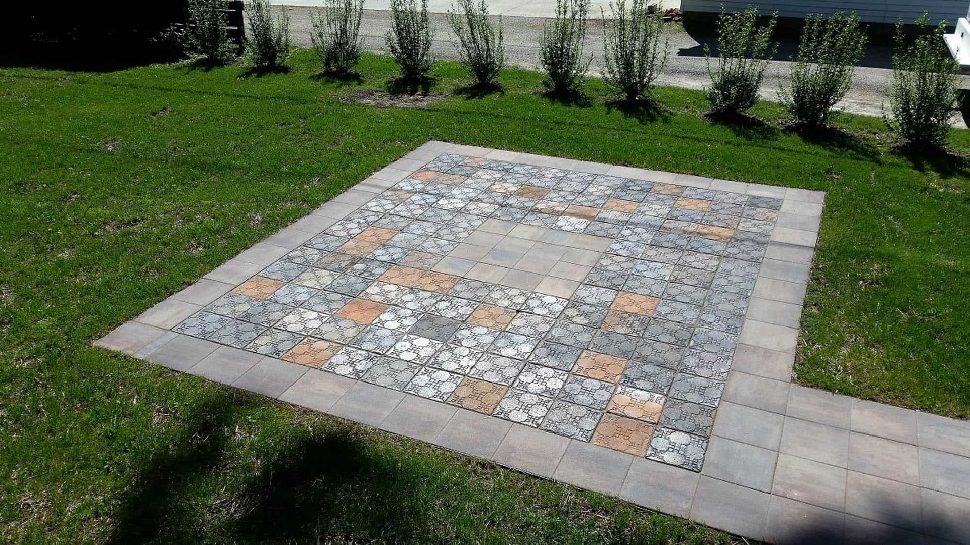 A patio with a pattern of tiles in the middle of a lush green field.