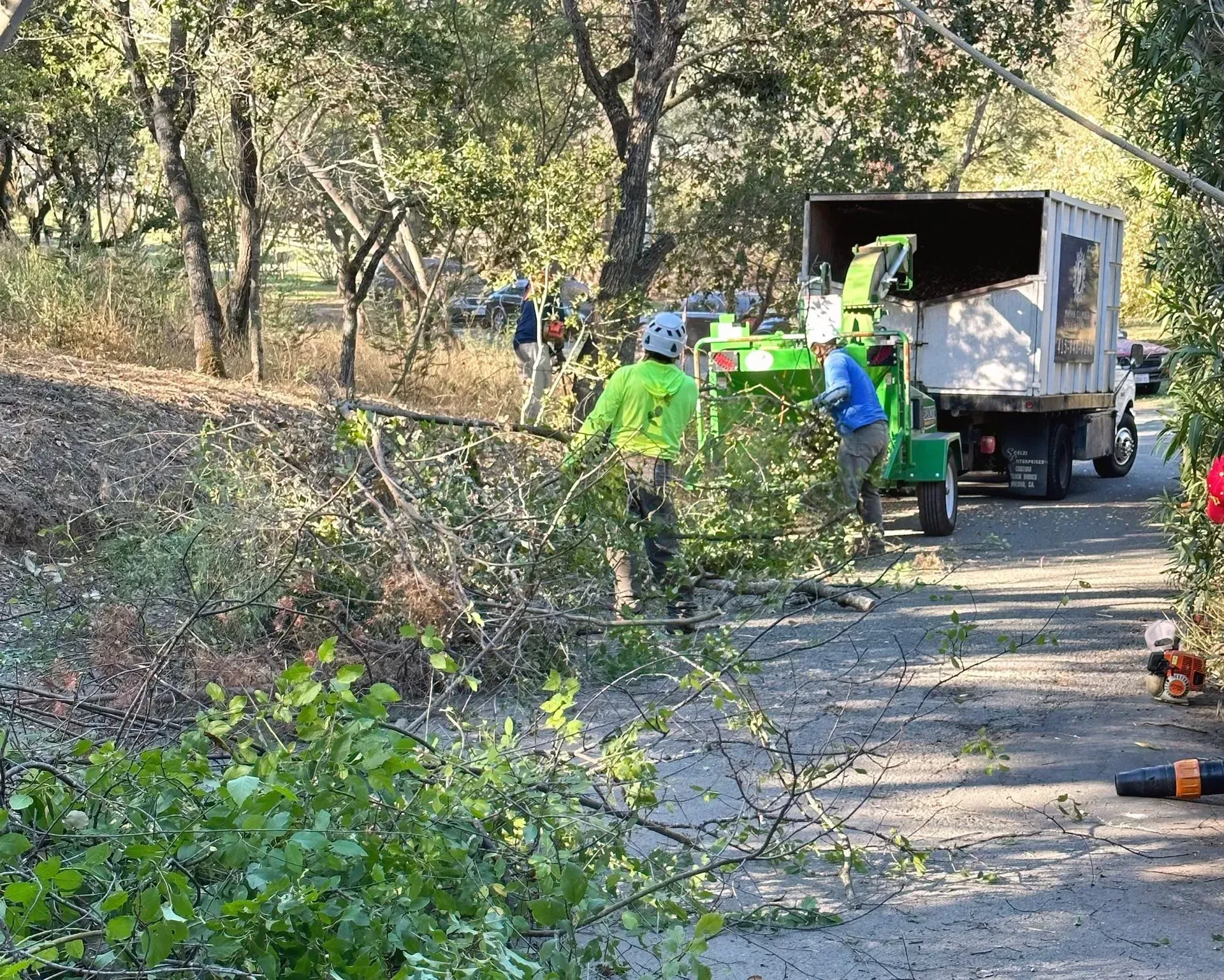 A group of people are working on a tree chipper in the woods.