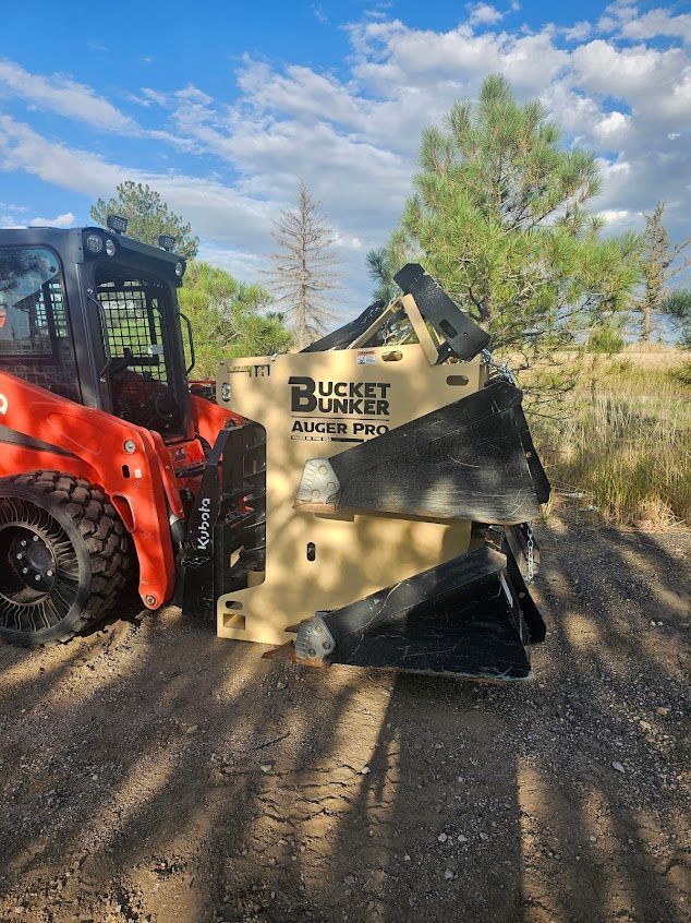 A red skid steer loader with a beige Bucket Bunker attachment on a dirt road, outdoors with a cloudy sky.