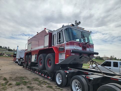 A large red and white fire truck is transported on a flatbed trailer. Cloudy sky in the background.