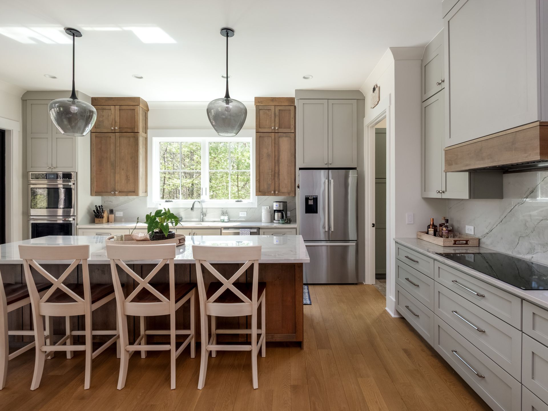 Modern kitchen with light wood floor, gray and wood cabinets, island with stools.