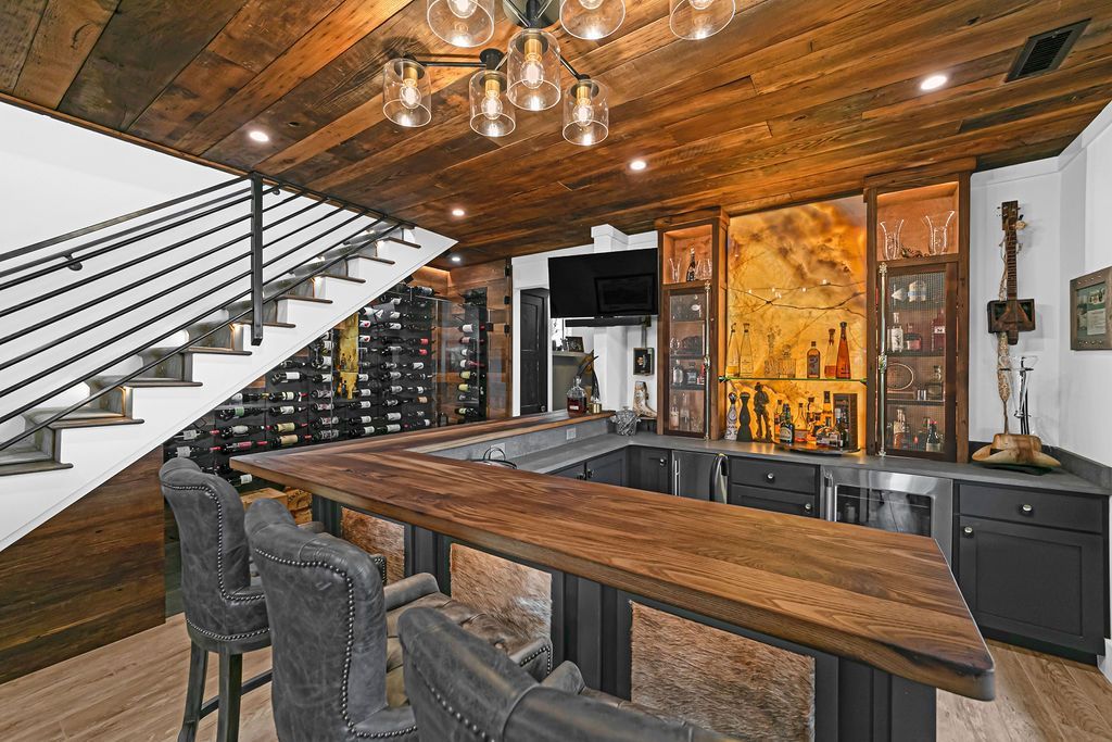 Rustic home bar with wood paneling, metal bar stools, and a staircase.