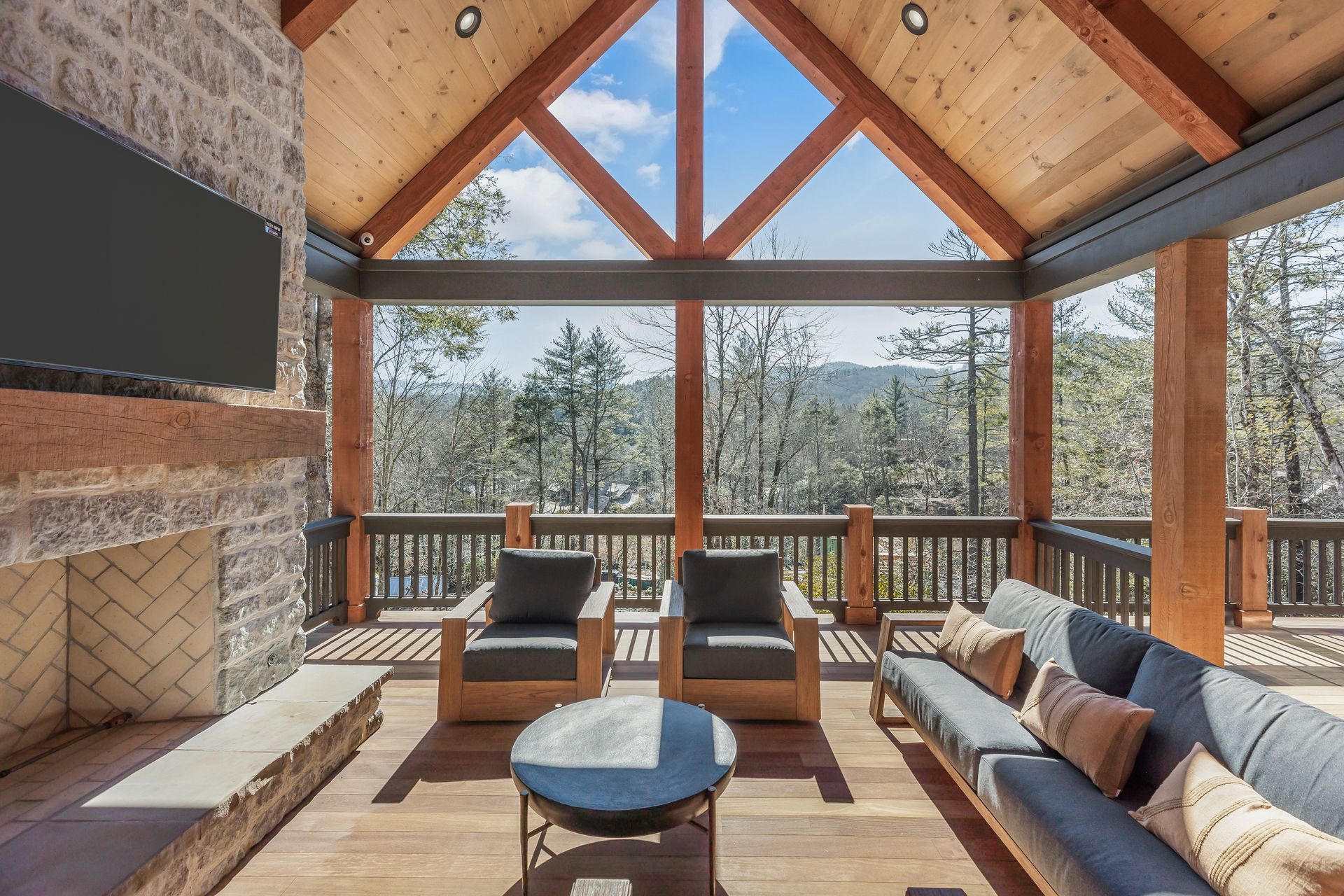 Outdoor covered patio with mountain view, seating, fireplace, and exposed wood beams.
