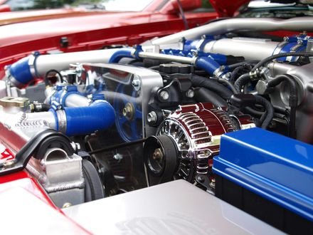 Close-up of a car engine bay with blue hoses, polished metal parts, and a red vehicle body