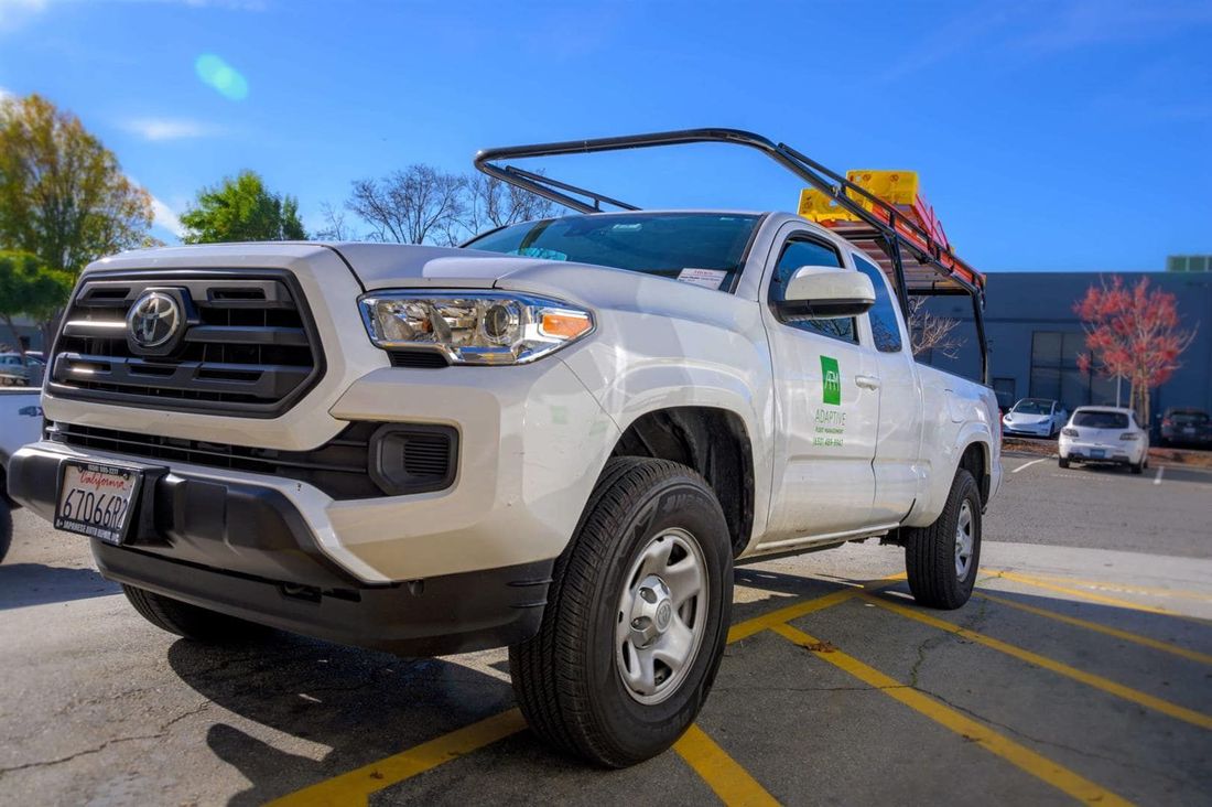 White pickup truck with ladder rack parked in a sunny lot near a building | Adaptive Fleet Management
