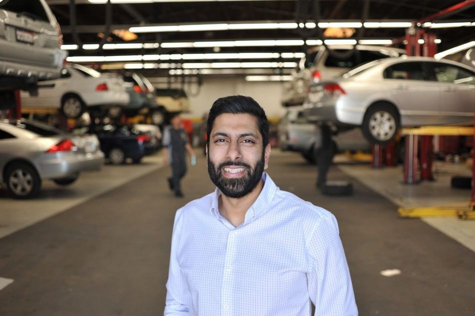 Man smiling in a car repair garage with vehicles on lifts in the background | Adaptive Fleet Management