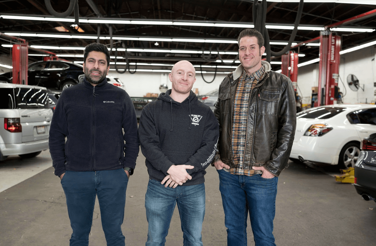 Three men standing in a parking garage between parked cars, facing the camera. | Adaptive Fleet Management