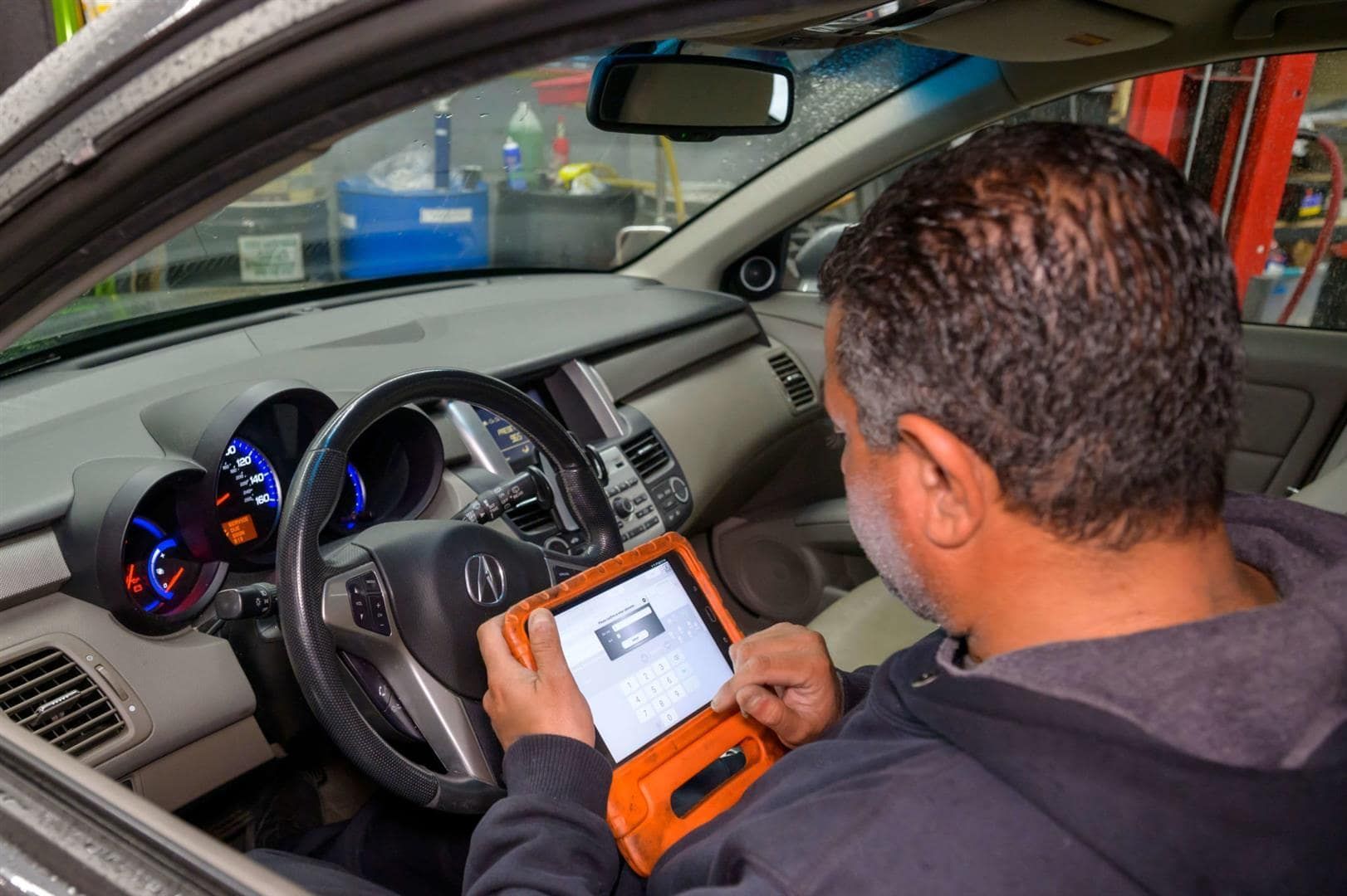 Mechanic using a diagnostic tablet inside a car, with the dashboard and steering wheel visible. | Adaptive Fleet Management