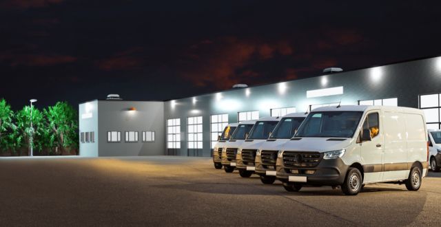 White cargo vans parked outside a lit industrial building at night | Adaptive Fleet Management