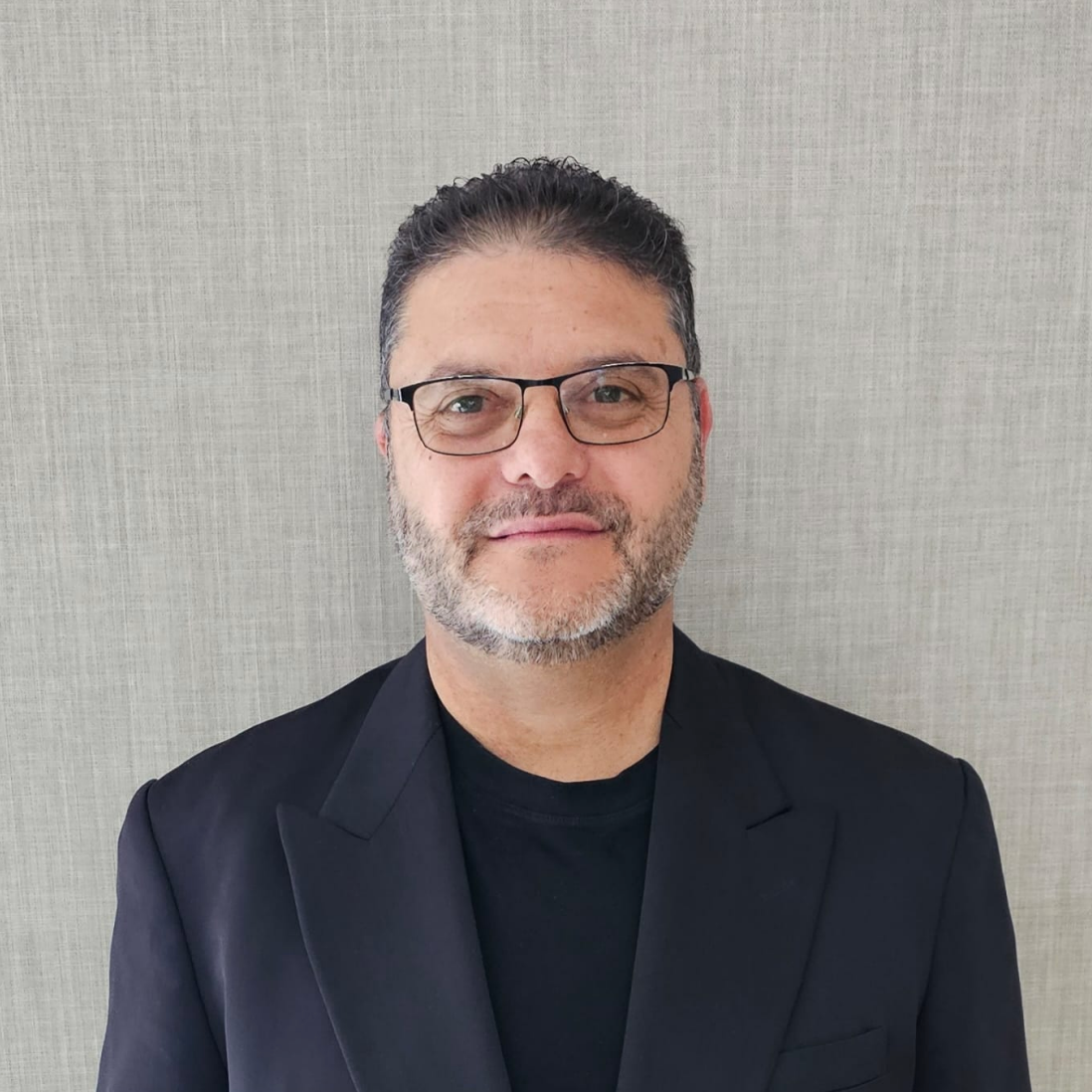 A man wearing glasses and a suit is standing in front of a wall.