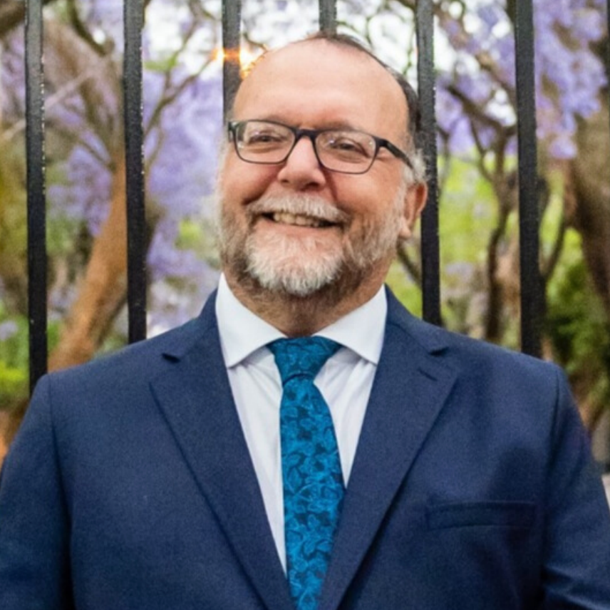 A man in a suit and tie is smiling in front of a fence.