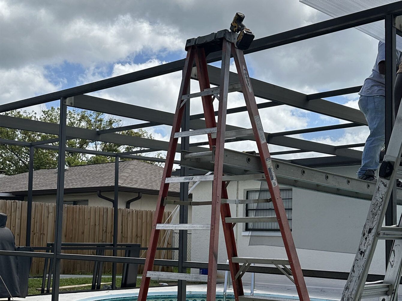 A man is standing on a ladder next to a pool.