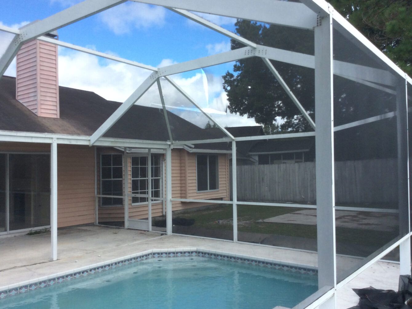 A screened in swimming pool with a house in the background