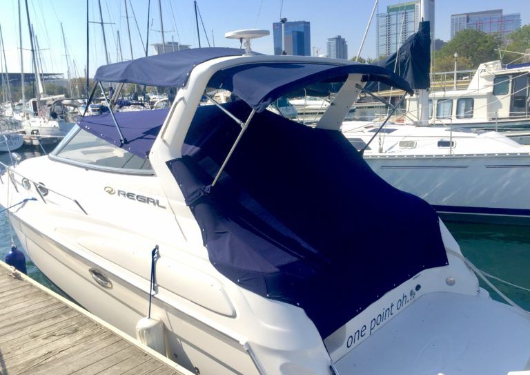 A white boat with a blue cover is docked at a marina