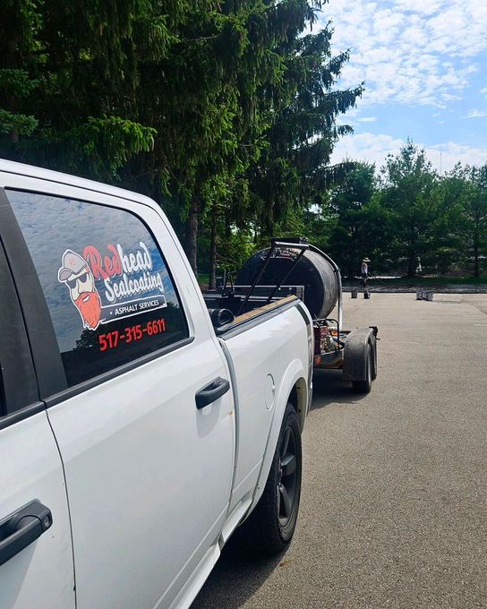 A white truck with a trailer attached to it is parked in a parking lot.