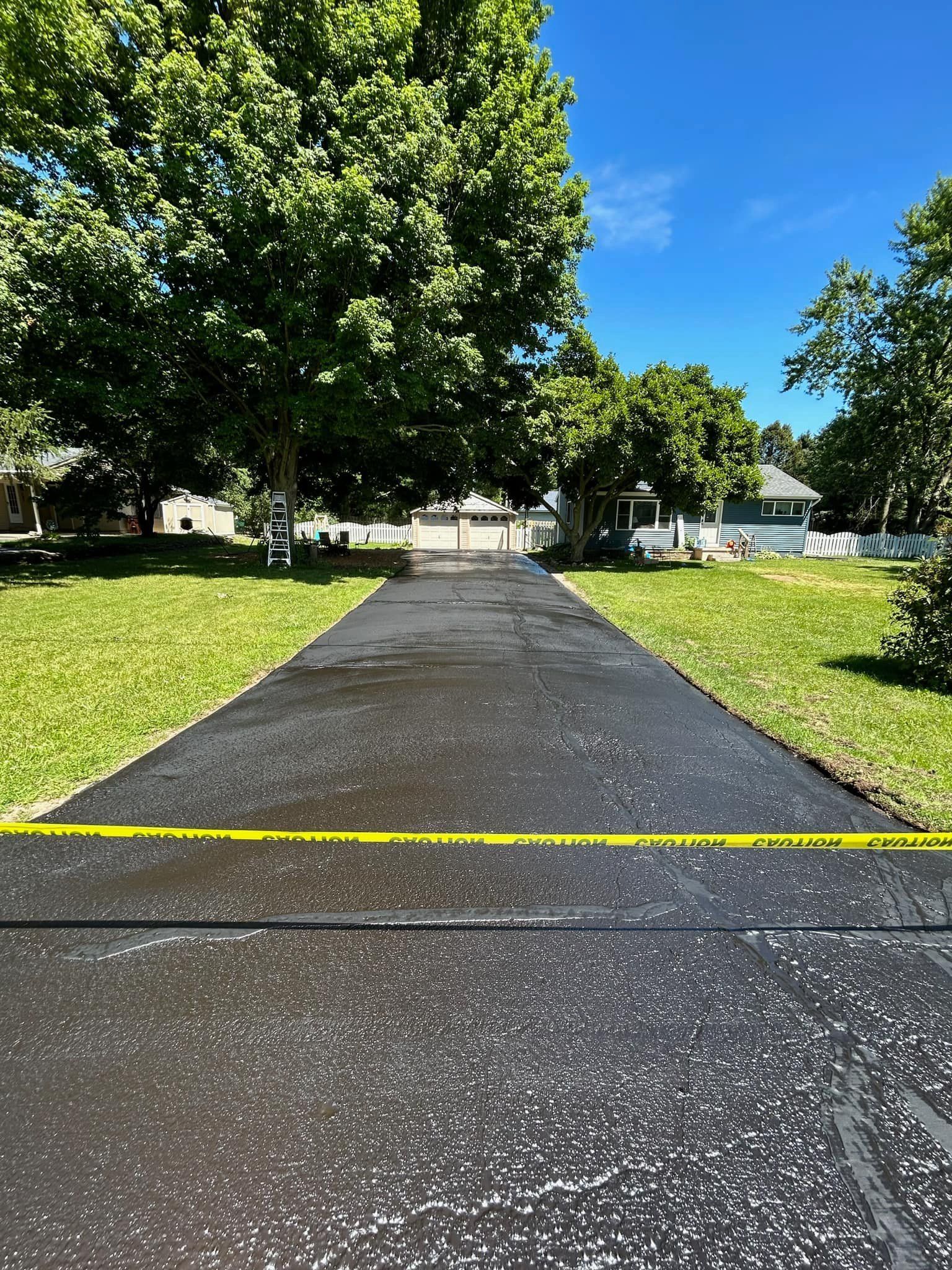 A black driveway leading to a house with trees on both sides.