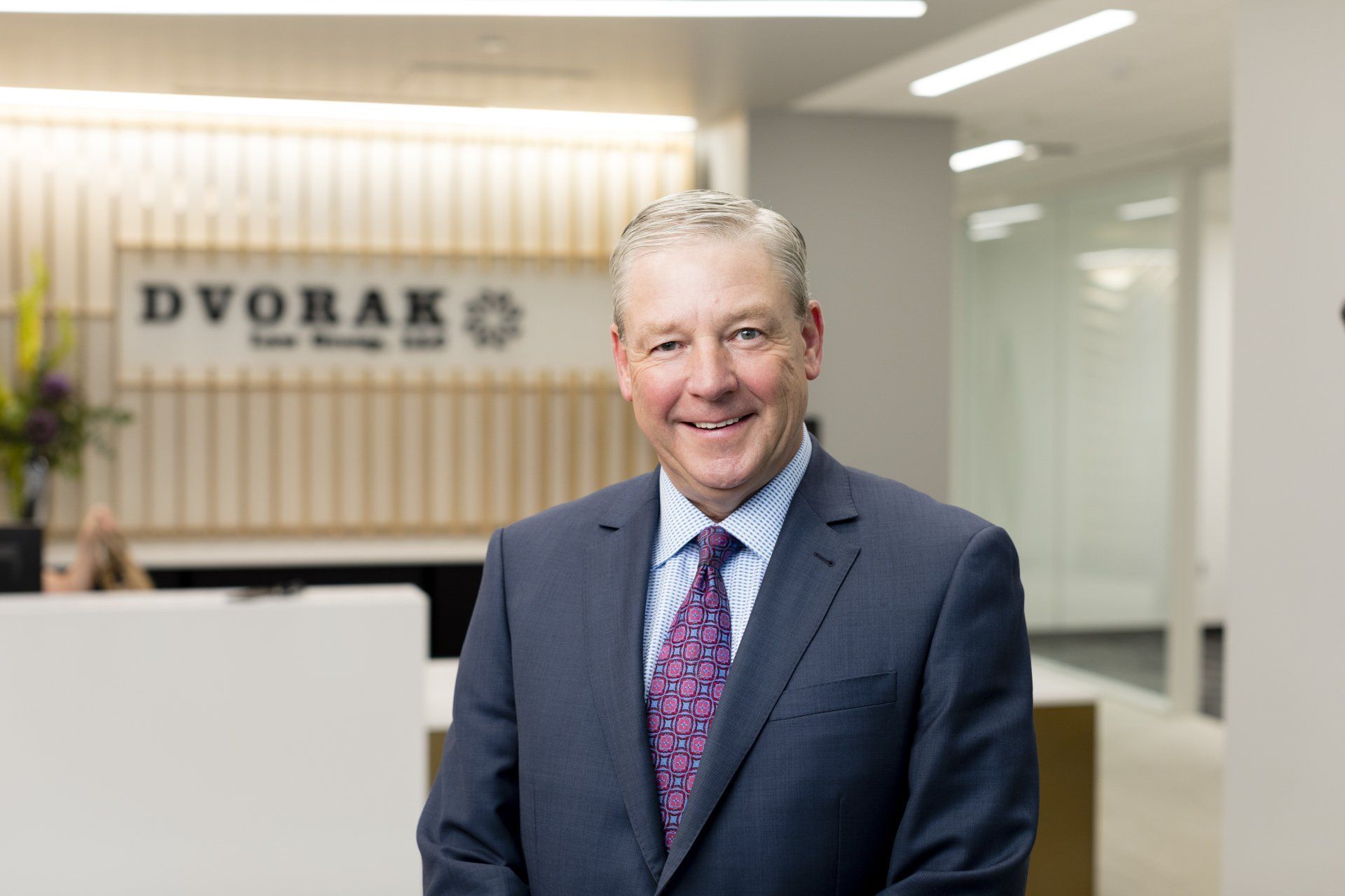 Smiling man in a suit stands in front of a reception desk with a Dvorak logo.