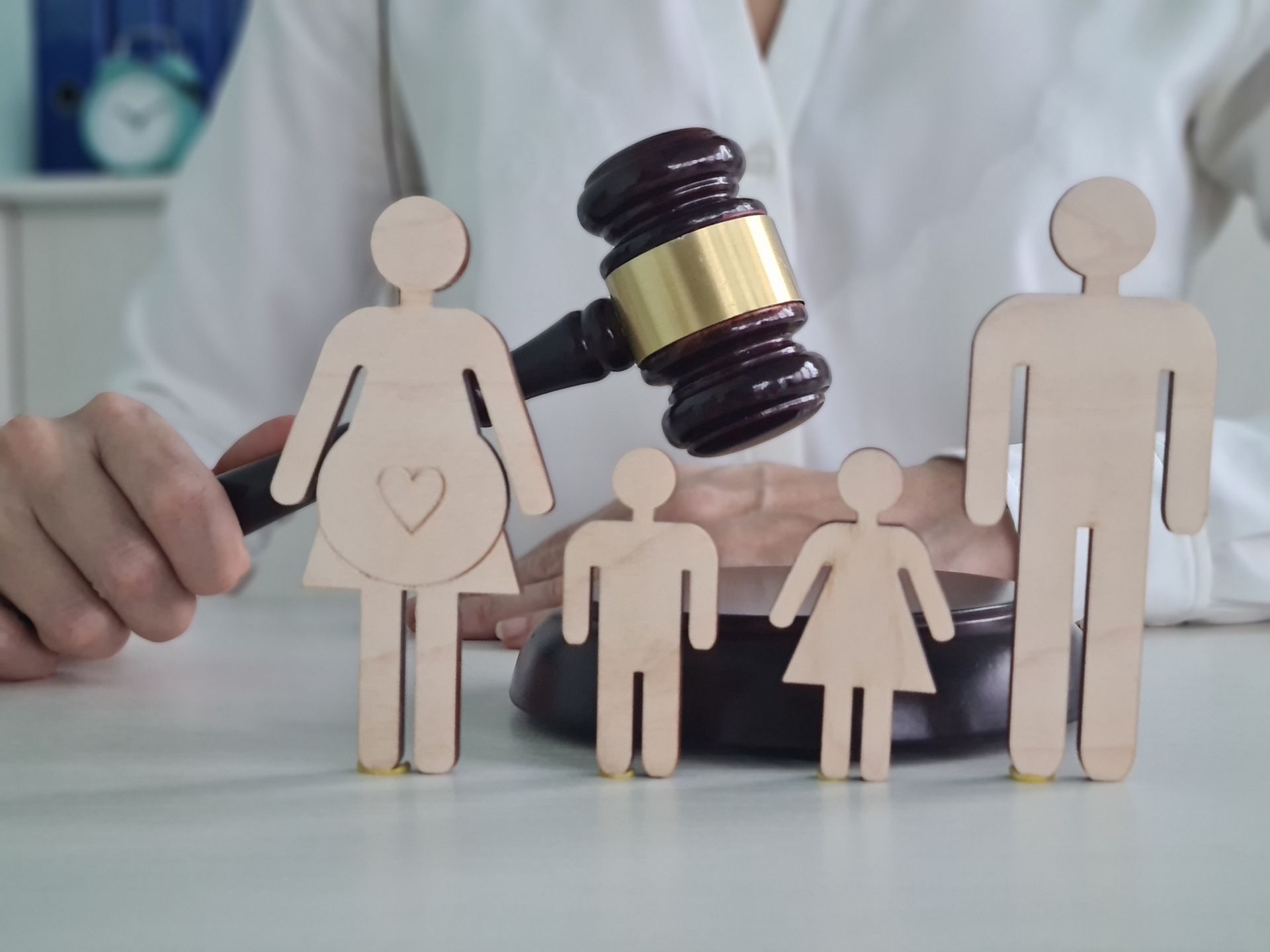 A child custody lawyer holds a gavel above wooden figures representing a family.