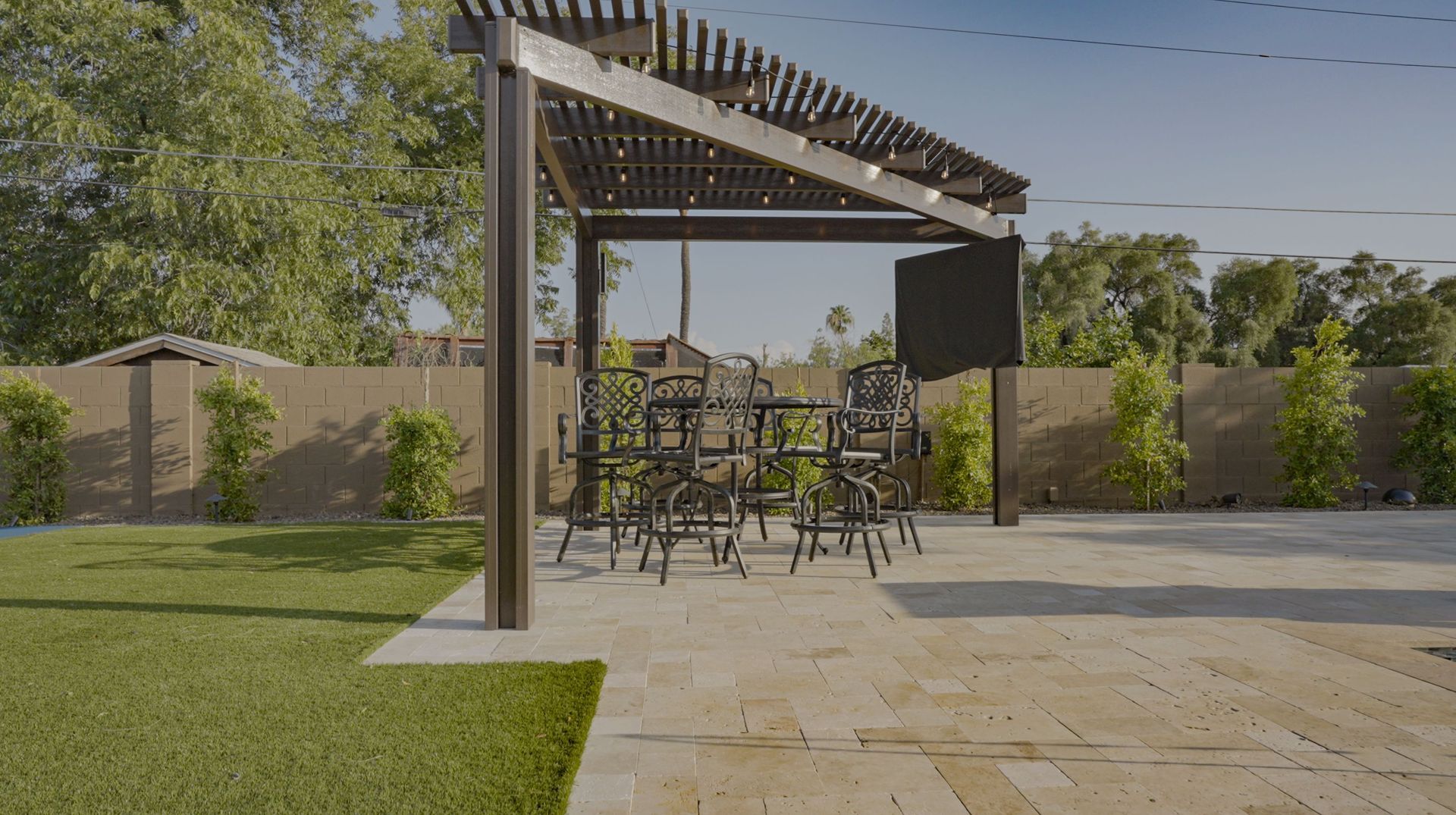 A patio with a table and chairs under a pergola in a backyard.