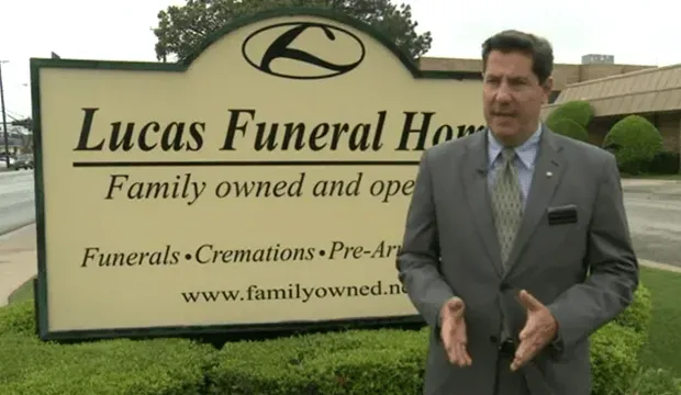 A man stands in front of a sign for lucas funeral home