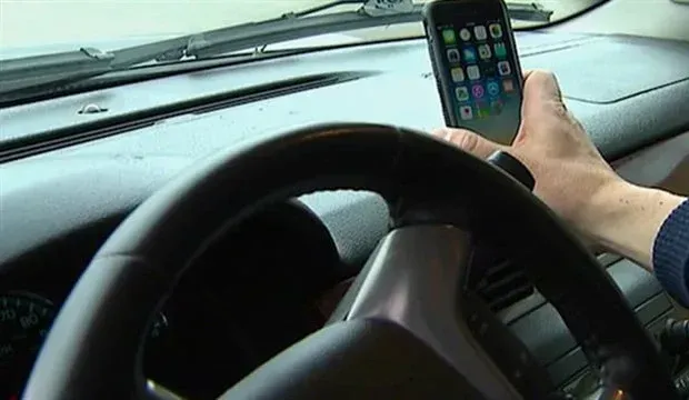 A person is holding a cell phone in their hand while driving a car.