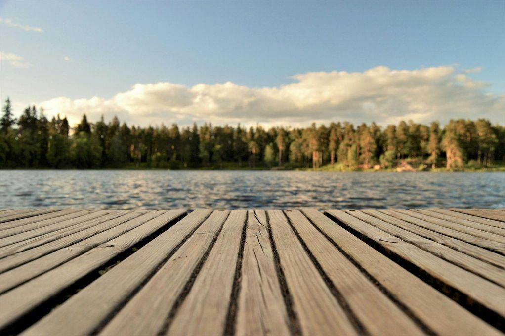 Wooden dock over a lake, forest in the background, blue sky with clouds.
