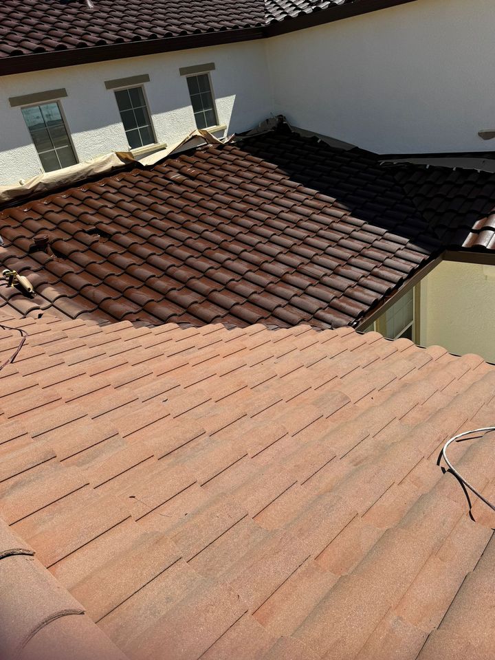 A high-angle view shows a roof with light tan concrete tiles in the foreground and dark brown tiles on a lower section.