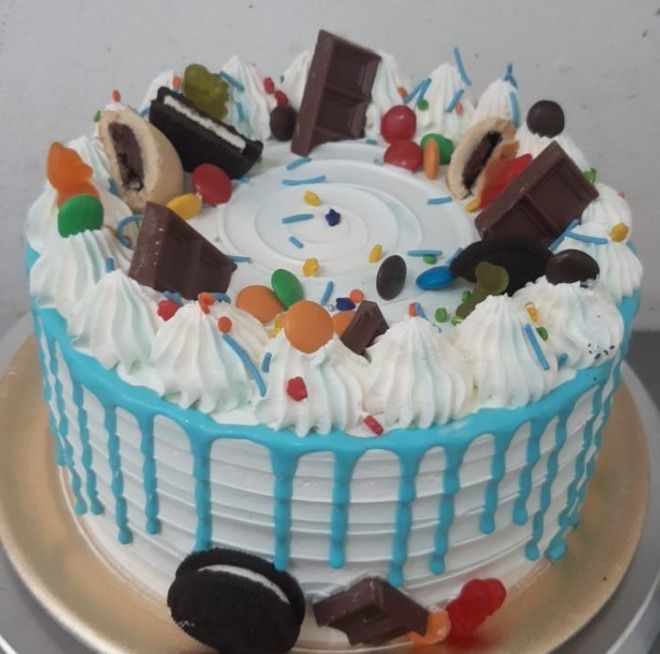 Pastel decorado con glaseado blanco, goteo azul, trozos de chocolate y dulces.