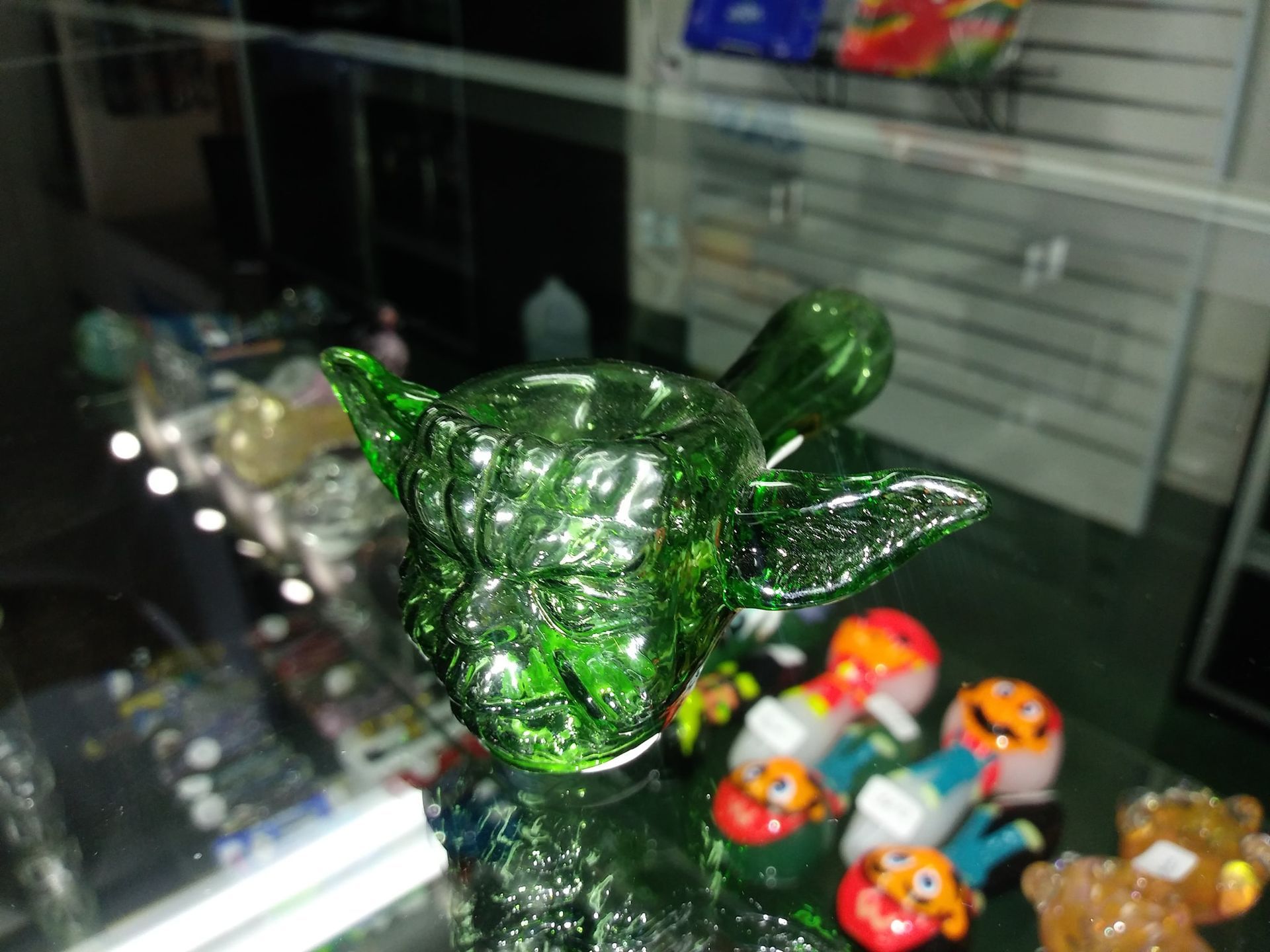 A green glass pipe in the shape of yoda is sitting on a glass table.