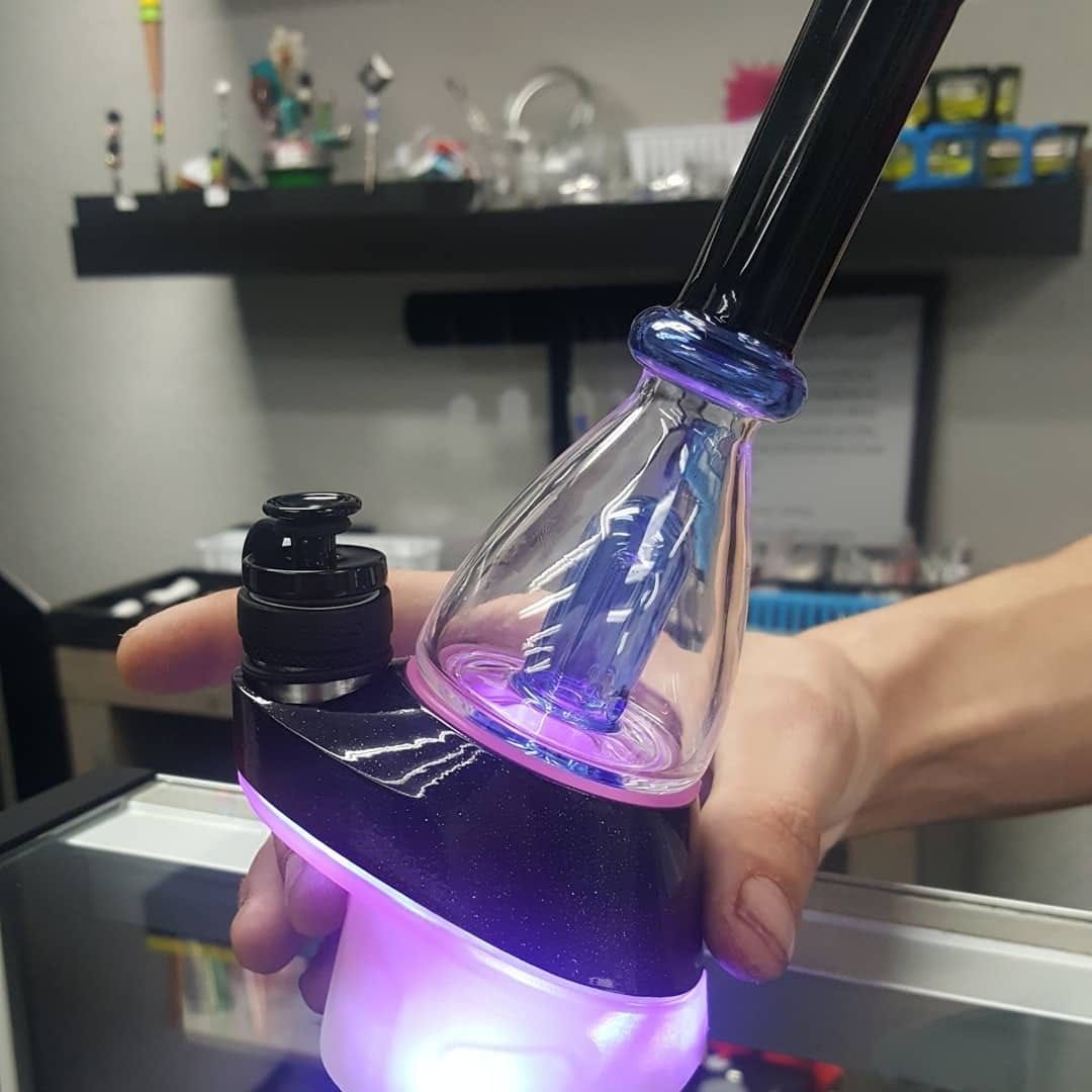 A person is holding a glass pipe with a purple light on it.