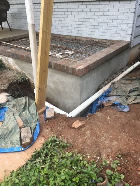 A wooden post is sitting in the dirt next to a brick wall.