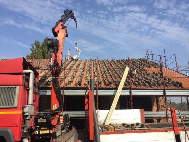 Gru che rimuove le tegole da un edificio. Camion rosso e impalcature visibili, giornata di sole.