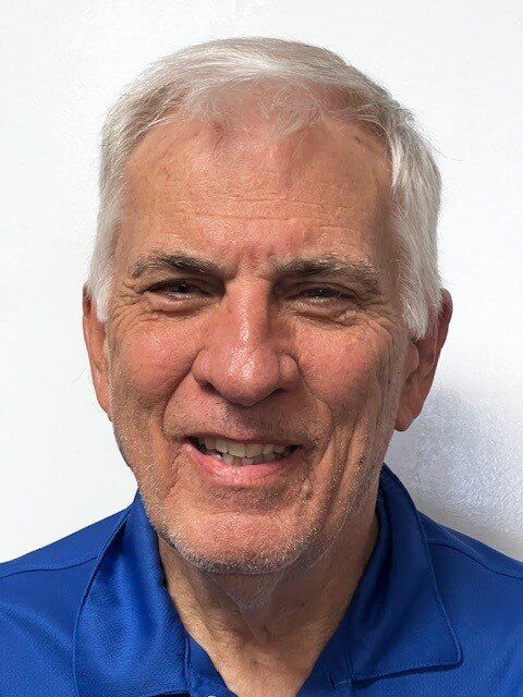Smiling older man with short white hair and blue shirt.
