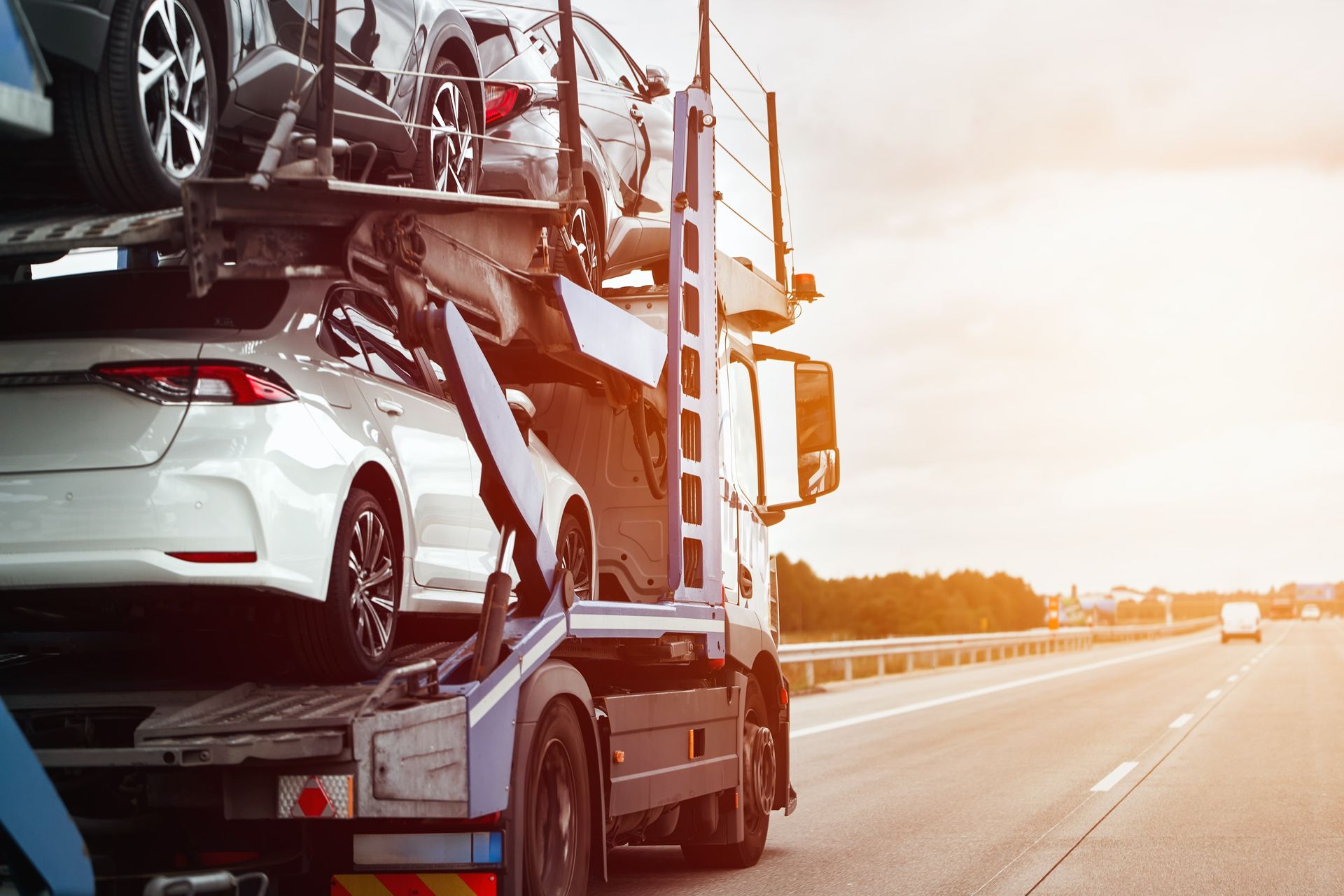 Car carrier truck transporting new vehicles on a highway at sunset.